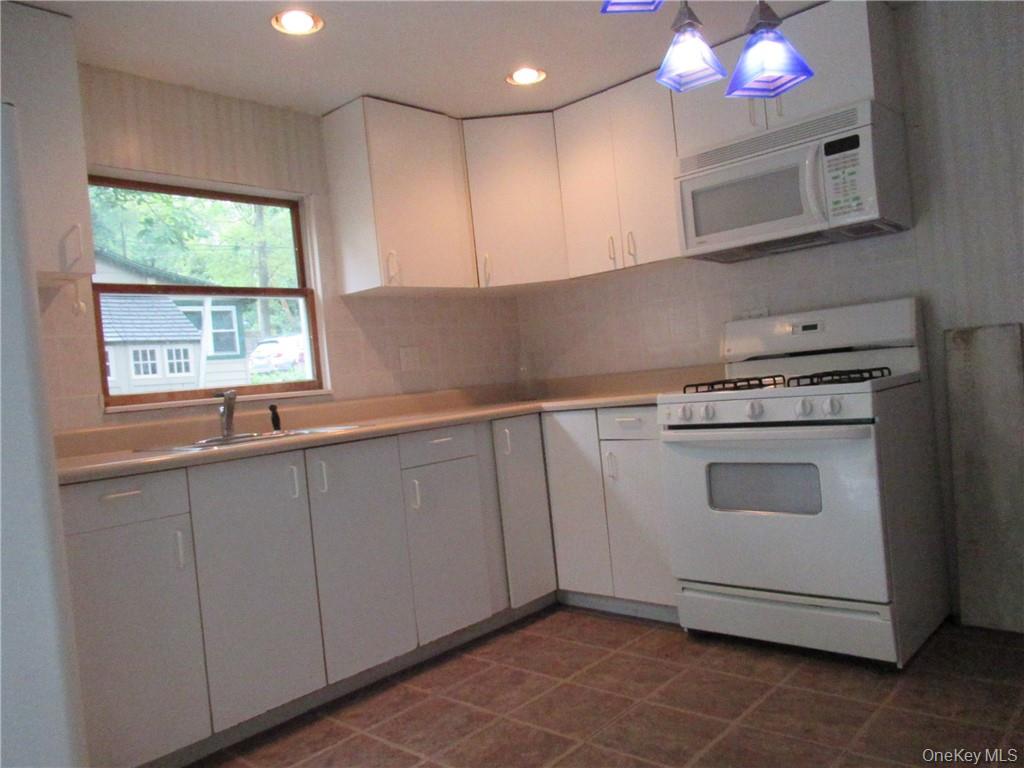 357 Mountain Lodge Road Monroe, NY 10950 - Photo 4 of 20 Kitchen featuring dark tile patterned floors, white appliances, white cabinets, backsplash, and sink