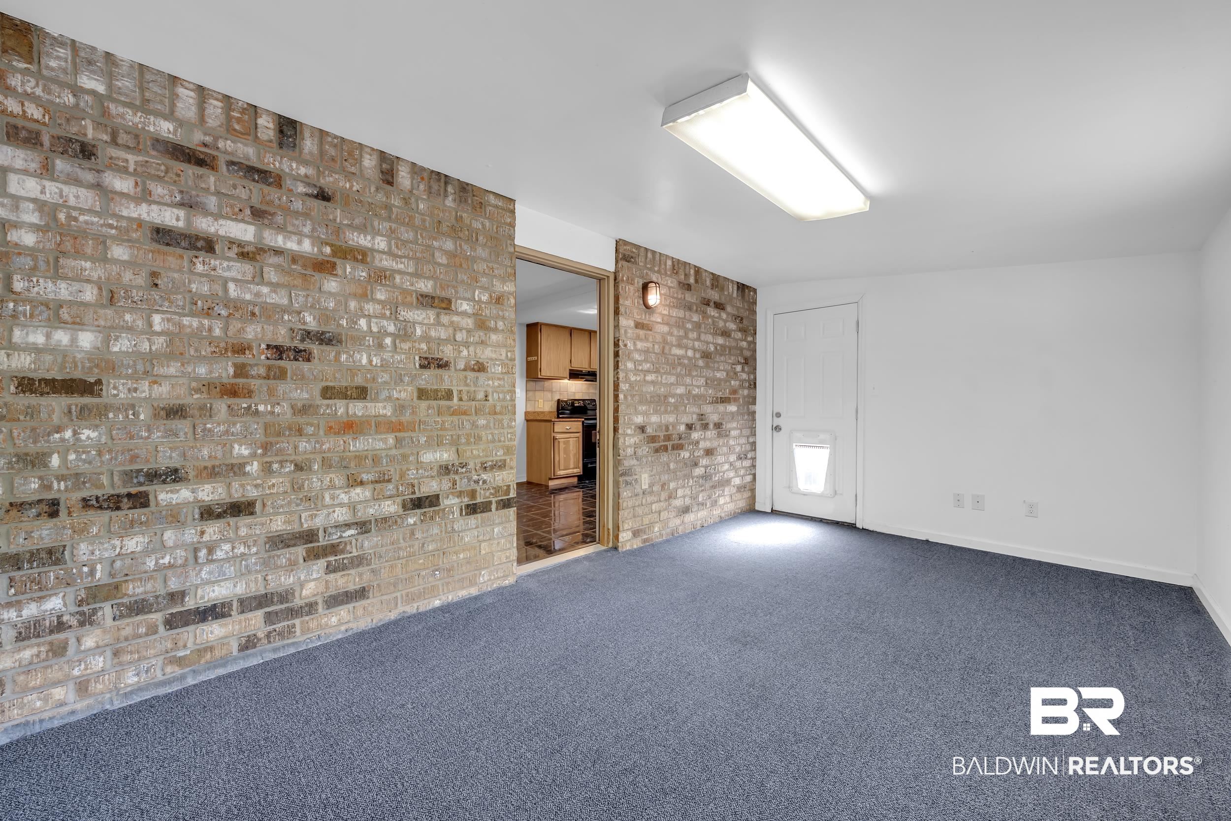 421 Cedar Court Foley, AL 36535 - Photo 25 of 39 Interior space featuring a brick accent wall, blue carpeting, white painted walls, and a fluorescent ceiling light fixture