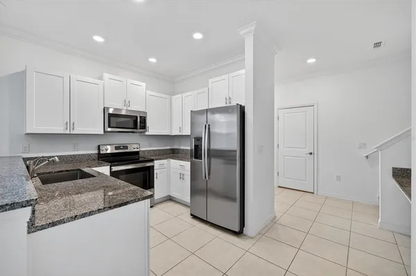 a kitchen with stainless steel appliances granite countertop a refrigerator a stove a sink and white cabinets