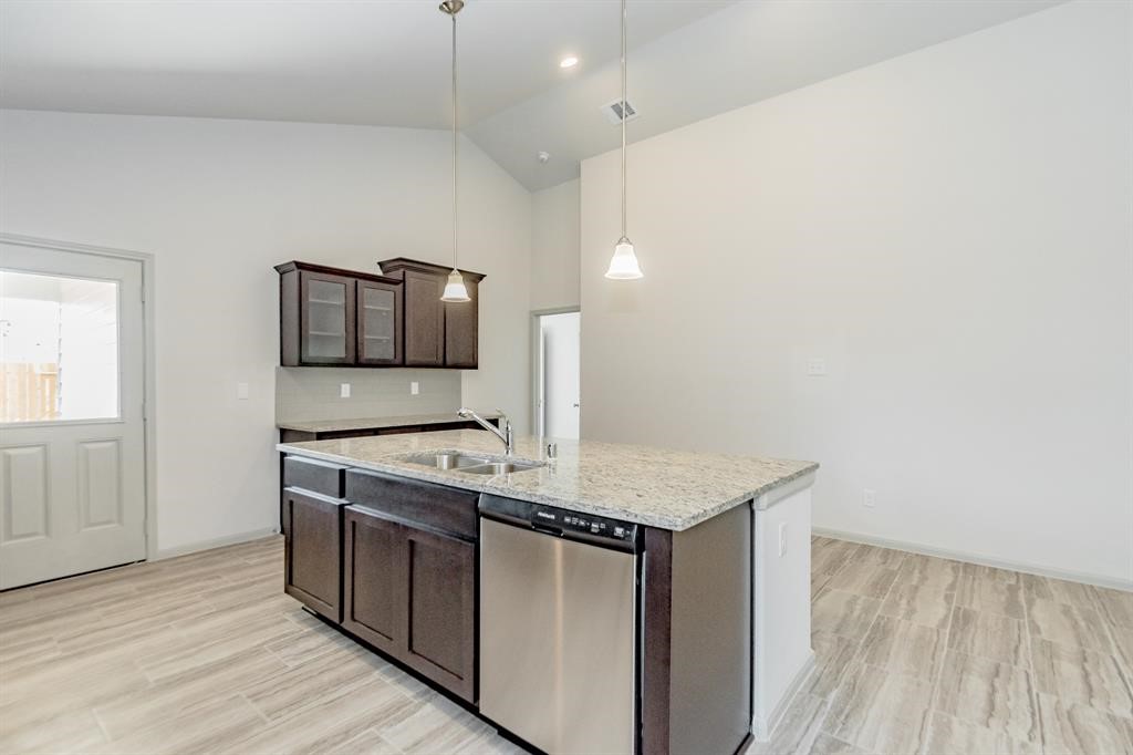 6447 Escondido Drive Rosharon, TX 77583 - Photo 16 of 16 Sleek, modern, and functional, this view highlights the spacious kitchen, featuring an oversized island with stunning quartz countertops and a built-in stainless-steel dishwasher. Elegant pendant lighting enhances the contemporary vibe, while ample cabinet space ensures optimal storage. With easy access to the backyard and an open floor plan, this kitchen is designed for effortless entertaining and everyday living.