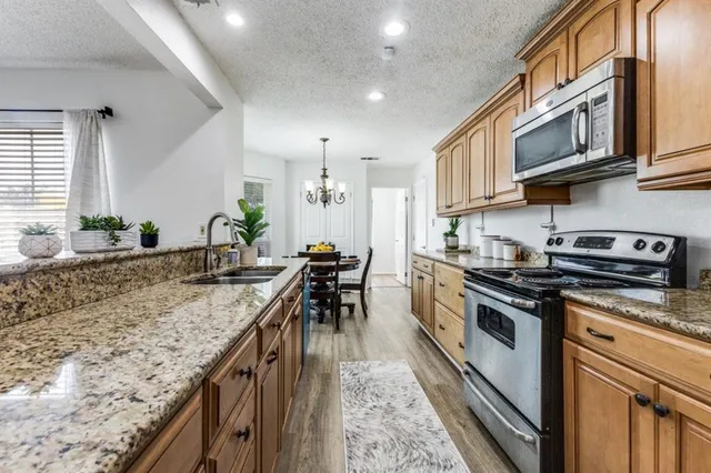 a kitchen with stainless steel appliances granite countertop a sink a stove and a wooden cabinets