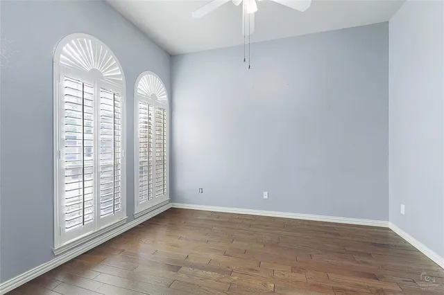 an empty room with wooden floor fan and windows