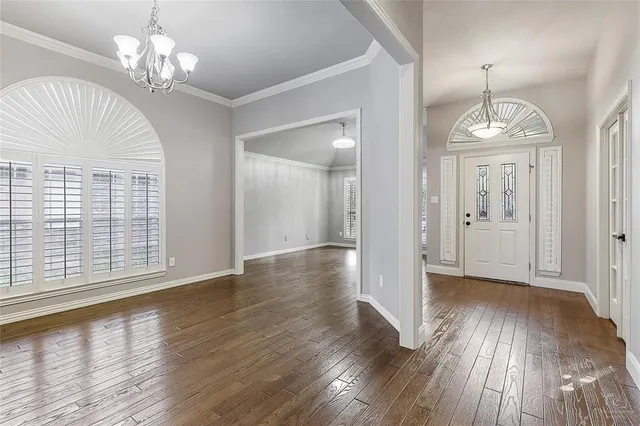 an empty room with wooden floor chandelier and windows