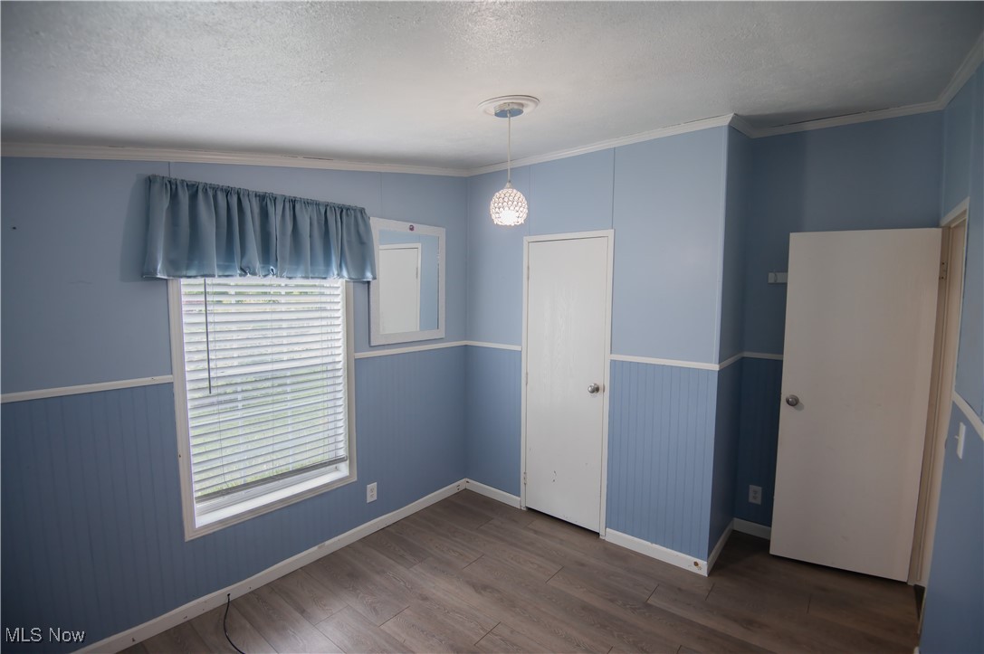 4594 Center Road Andover, OH 44003 - Photo 24 of 39 Unfurnished bedroom featuring crown molding, dark wood-style flooring, a textured ceiling, and wainscoting
