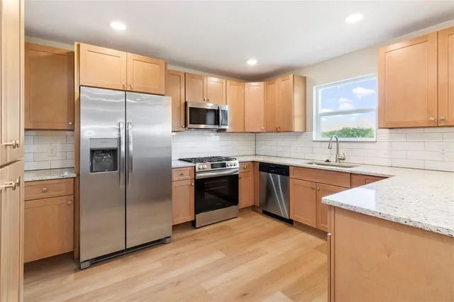 a kitchen with stainless steel appliances granite countertop a refrigerator a sink dishwasher a stove top oven a refrigerator with white cabinets and wooden floor