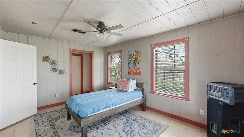 127 Offer Llano, TX 78643 - Photo 20 of 40 Room featuring vertical board paneling, a paneled ceiling, two windows with contrasting trim, and a ceiling fan with light fixture