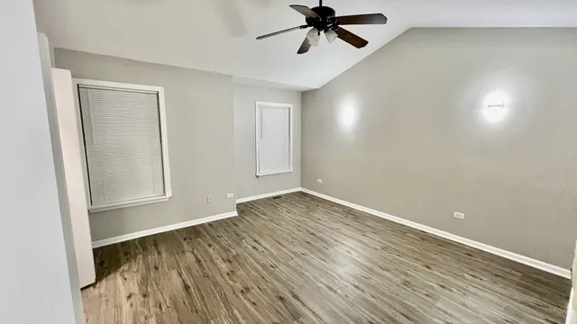 an empty room with wooden floor fan and windows