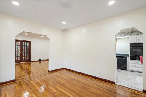 an empty room with wooden floor and way to kitchen
