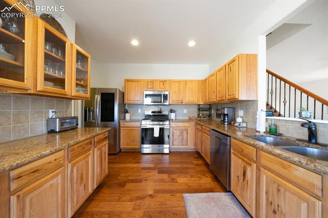 907 Spectrum Loop Colorado Springs, CO 80921 - Photo 8 of 44 Kitchen featuring appliances with stainless steel finishes, stone countertops, hardwood / wood-style floors, backsplash, and sink