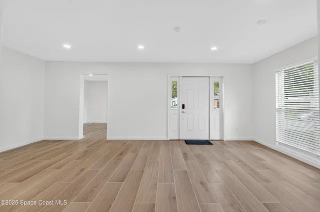 a view of an empty room with wooden floor and a window