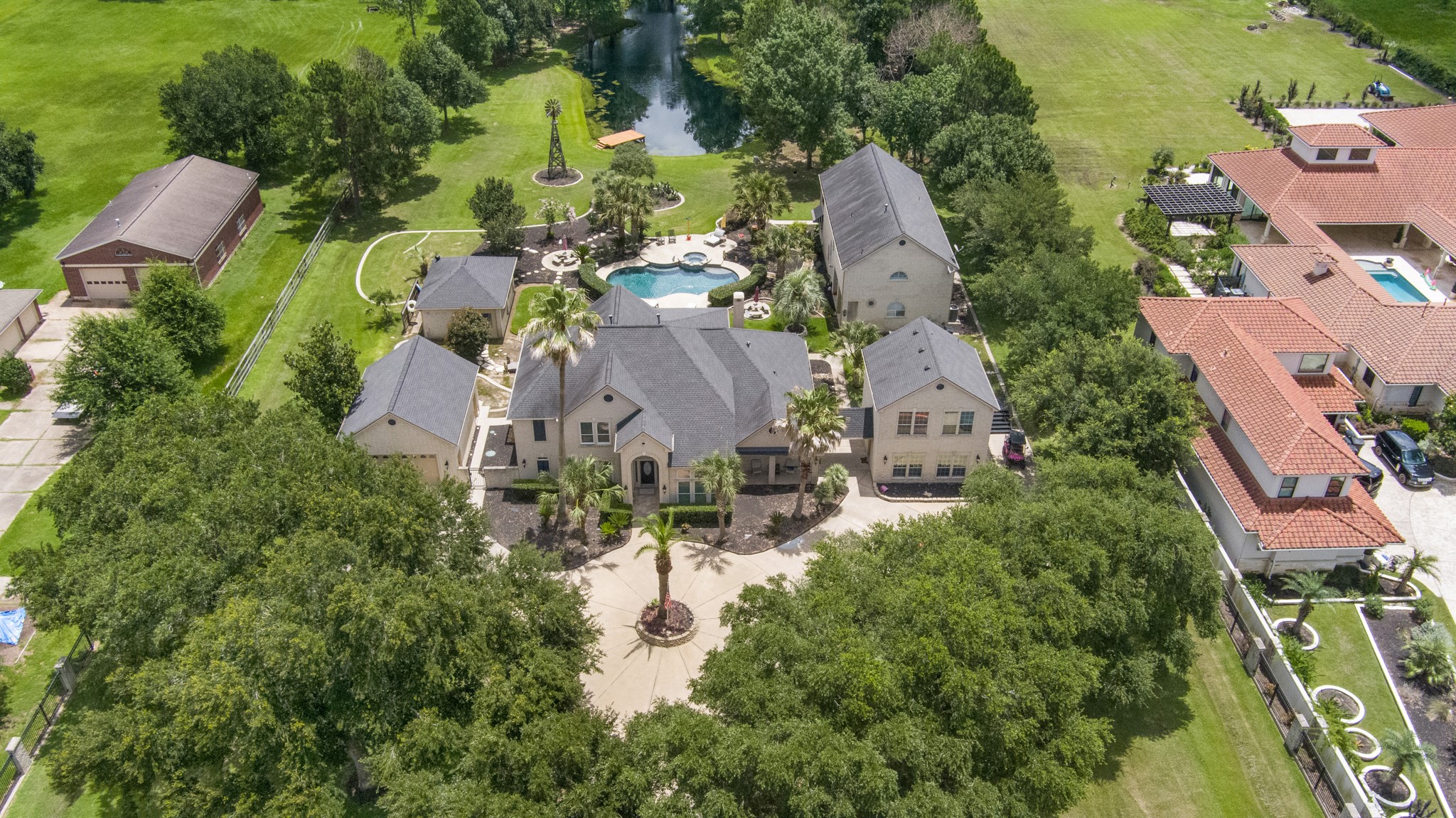 13914 Skinner Road Cypress, TX 77429 - Photo 3 of 50 Elevated aerial view highlighting the estate’s expansive layout, multiple residences, resort style pool and spa, mature trees, manicured grounds, decorative windmill, and private pond.