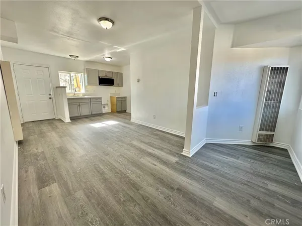 an empty room with wooden floor and a kitchen