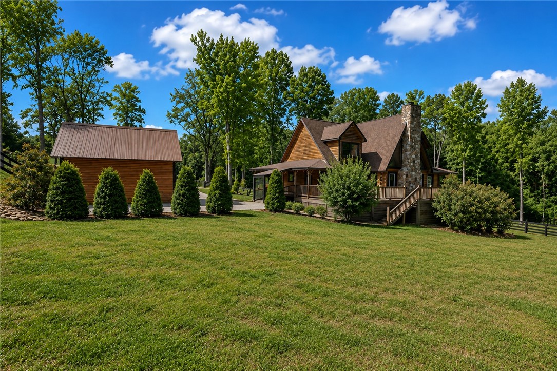 414 Devon Way Anderson, SC 29621 - Photo 37 of 50 A charming log home with an inviting porch and a detached barn is nestled among lush green trees.