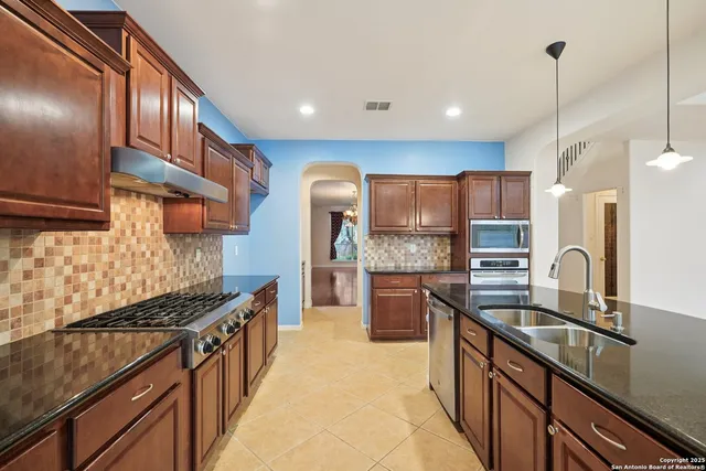 a kitchen with stainless steel appliances granite countertop a sink a stove and a wooden cabinets
