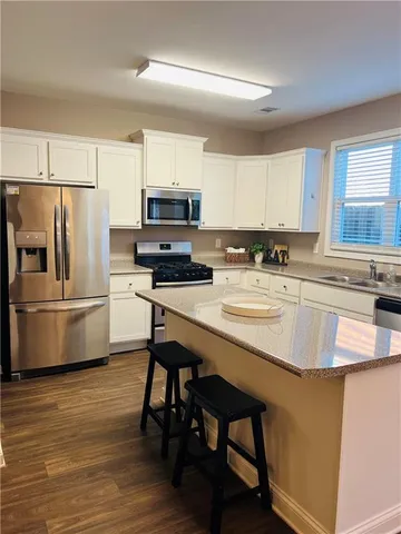 a kitchen with stainless steel appliances a stove a sink a microwave a refrigerator and white cabinets