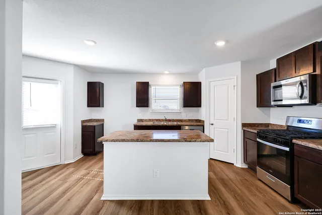 a kitchen with stainless steel appliances a stove top oven a sink a refrigerator white cabinets and wooden floor