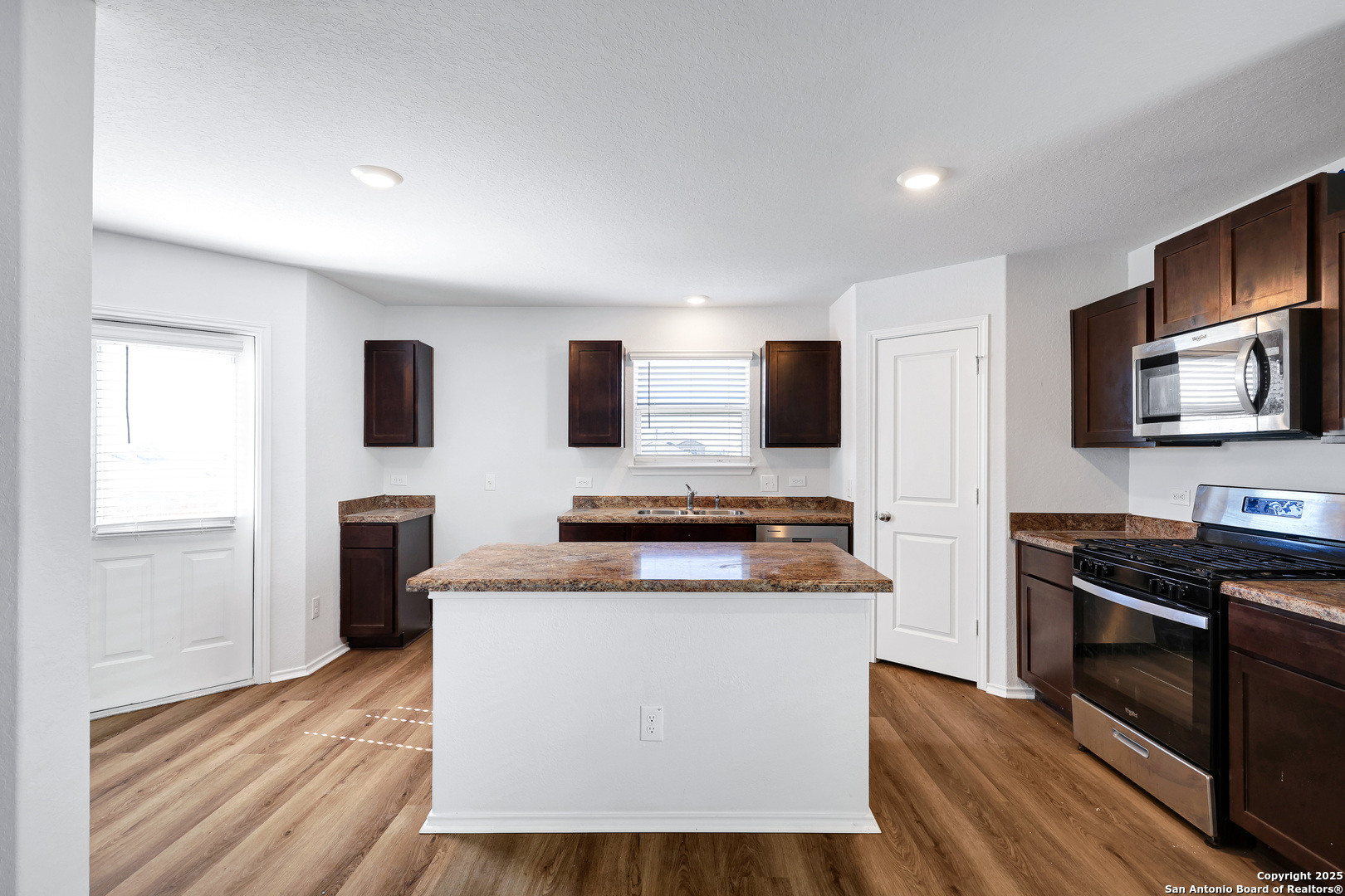 5867 Kendall Prairie San Antonio, TX 78244 - Photo 8 of 25 a kitchen with stainless steel appliances a stove top oven a sink a refrigerator white cabinets and wooden floor