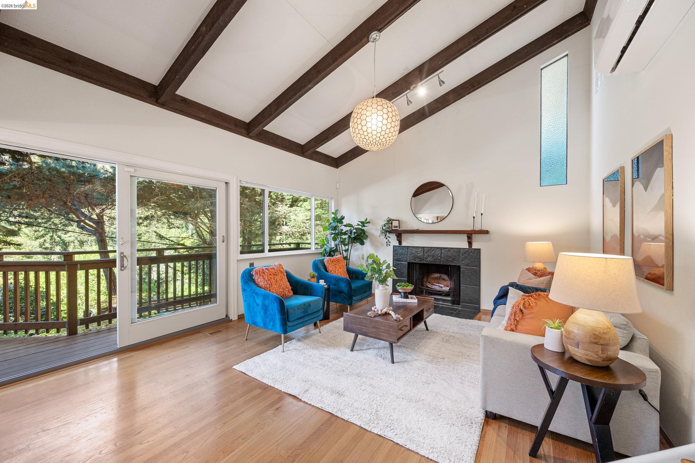 6600 Heather Ridge Way Oakland, CA 94611 - Photo 7 of 66 Spacious living area featuring a vaulted ceiling with exposed wood beams, wood-finish flooring, a fireplace with dark tile surround, and expansive glass sliding doors opening to an outdoor deck