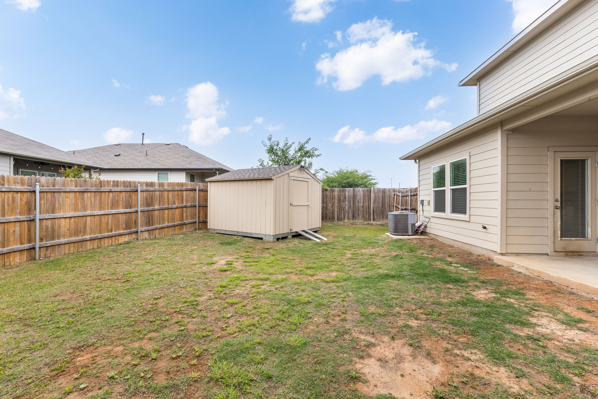 281 Jayden Drive Kyle, TX 78640 - Photo 30 of 36 Fenced backyard featuring a storage shed, covered patio, and a light-colored exterior wall with a window and a glass-paneled door