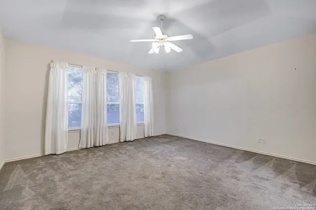 an empty room with chandelier fan and windows
