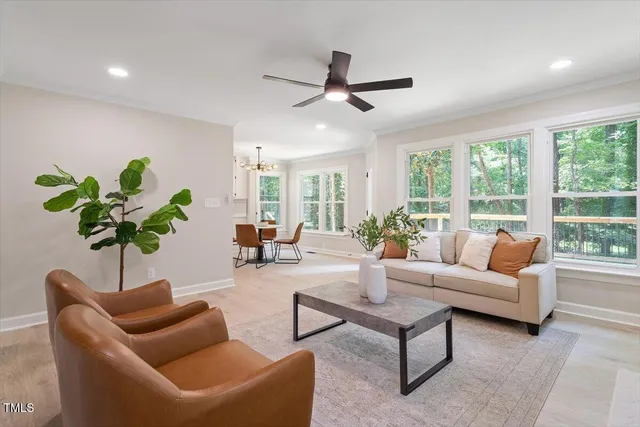 a living room with furniture a ceiling fan a potted plant and a large window