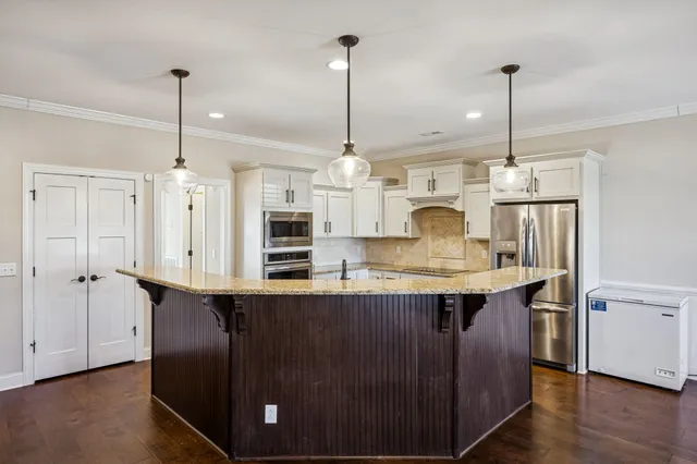 a kitchen with stainless steel appliances granite countertop a sink a island a stove a refrigerator and white cabinets