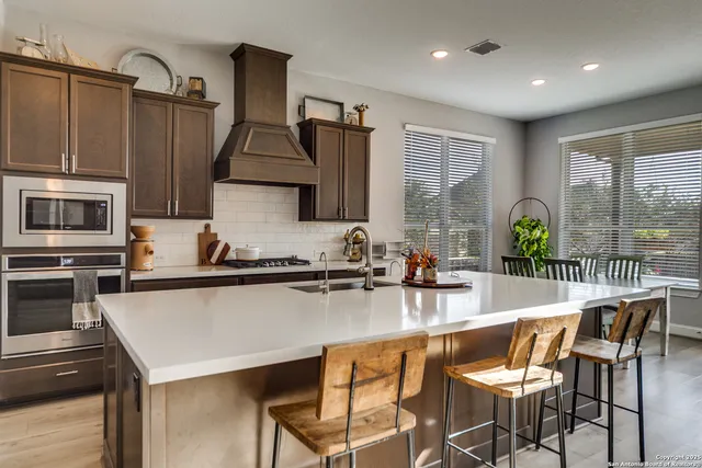 a kitchen with stainless steel appliances granite countertop a stove top oven a sink a dining table and chairs