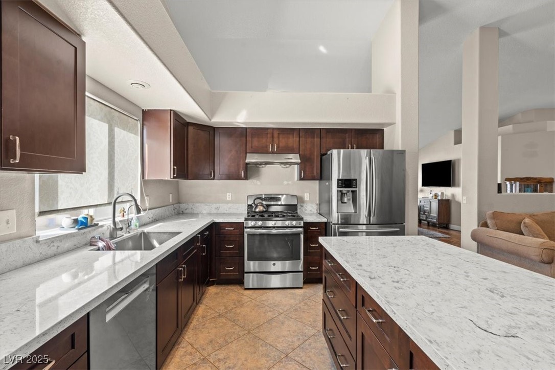 9031 West Viking Road Las Vegas, NV 89147 - Photo 17 of 33 Kitchen with light stone countertops, under cabinet range hood, dark brown cabinetry, appliances with stainless steel finishes, and a sink