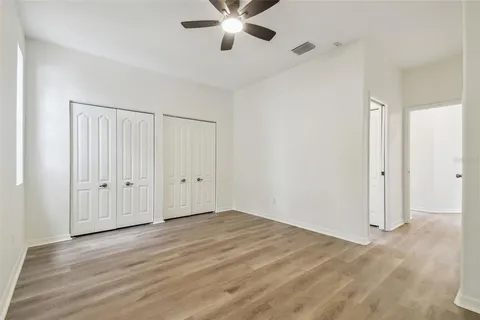 an empty room with wooden floor ceiling fan and windows