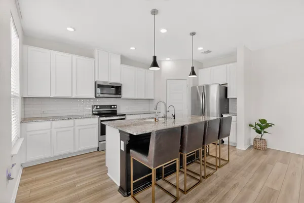 a kitchen with stainless steel appliances granite countertop a stove a refrigerator a kitchen island a sink and white cabinets with wooden floors