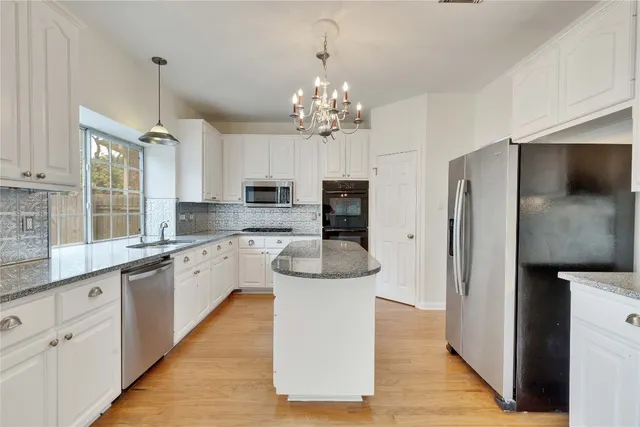 a kitchen with stainless steel appliances kitchen island granite countertop a refrigerator a sink dishwasher a oven with white cabinets and wooden floor