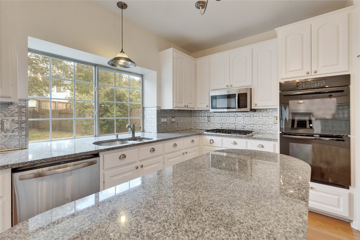 5407 Merrywing Circle Austin, TX 78730 - Photo 13 of 36 Kitchen with appliances with stainless steel finishes, light stone counters, hanging light fixtures, white cabinets, and backsplash