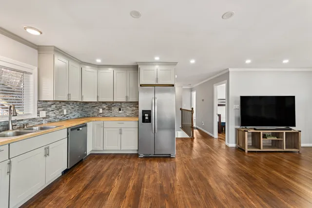 a kitchen with stainless steel appliances a refrigerator a sink dishwasher a oven with white cabinets and wooden floor