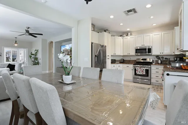 a kitchen with stainless steel appliances granite countertop a refrigerator a stove top oven a sink a dining table and chairs with wooden floor