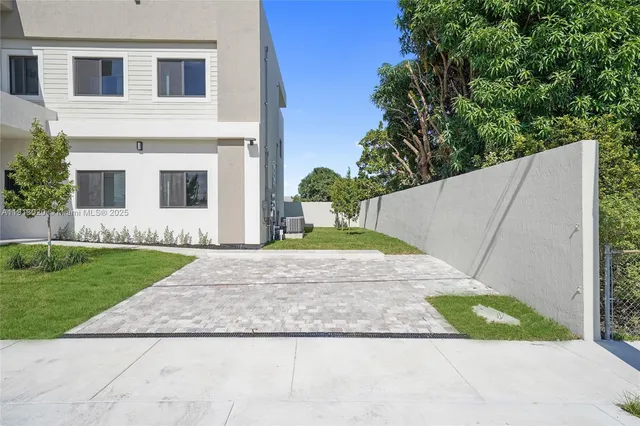 a view of a white house with a large windows and a yard with plants and large trees