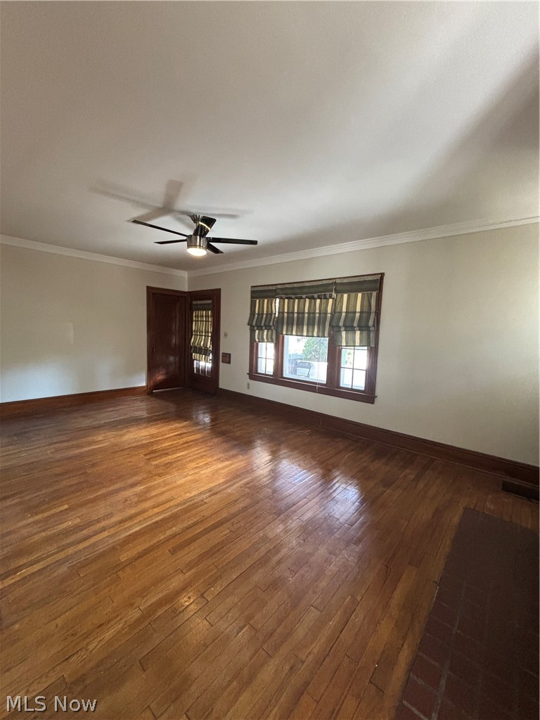 Hardwood flooring, crown molding, ceiling fan with integrated lighting, wood-frame windows, and a tiled hearth