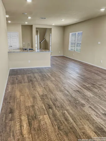 an empty room with wooden floor and kitchen view