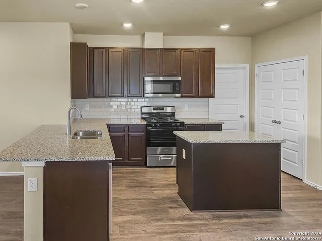 a kitchen with kitchen island granite countertop a stove top oven a sink dishwasher and wooden cabinets