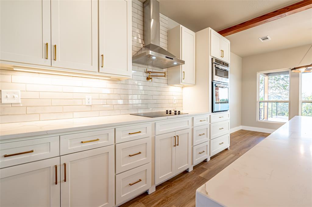 2128 Eagles Rdg Drive Weatherford, TX 76087 - Photo 31 of 39 Kitchen with wall chimney range hood, light stone counters, white cabinetry, tasteful backsplash, and beam ceiling