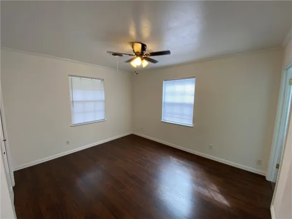 an empty room with wooden floor ceiling fan and windows