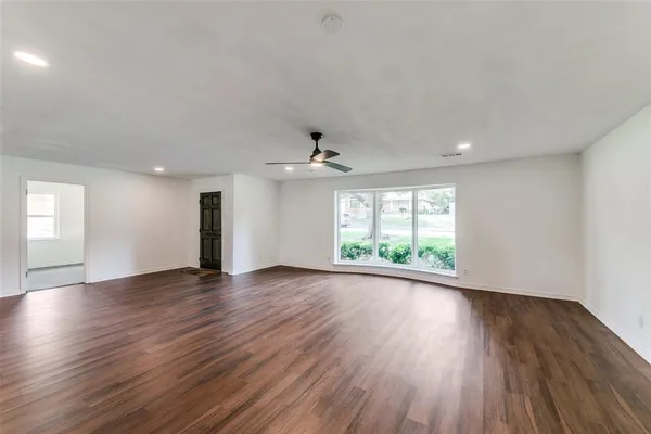a view of an empty room with wooden floor and a window