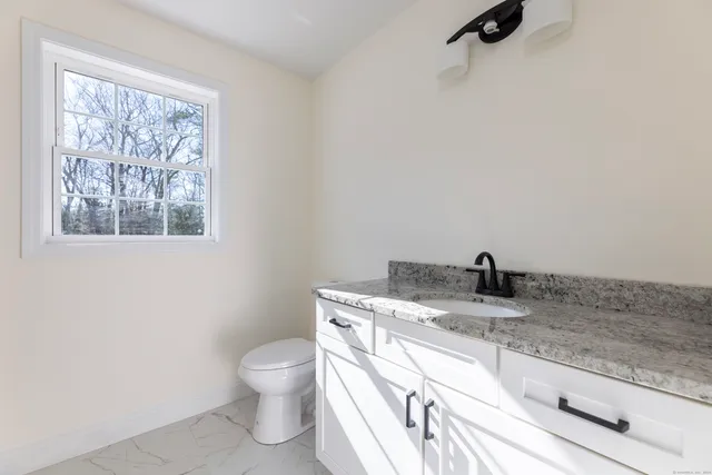 a bathroom with a granite countertop sink a toilet and a window