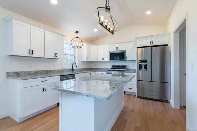 a kitchen with stainless steel appliances granite countertop a refrigerator a stove a sink and white cabinets