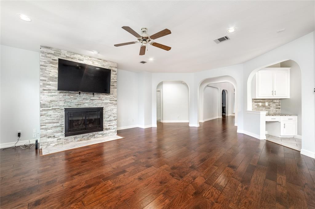 5801 Yeary Road Plano, TX 75093 - Photo 9 of 33 Spacious living area featuring wood-finish flooring, a stone-clad fireplace, and a ceiling fan