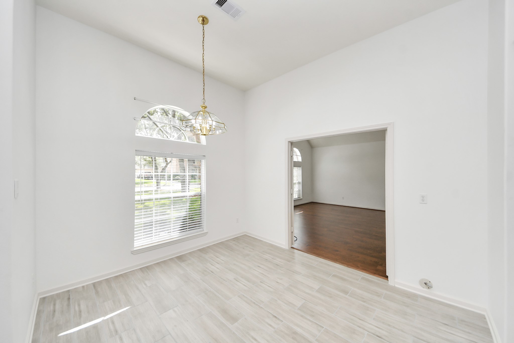 5815 Pheasant Ridge Lane Houston, TX 77041 - Photo 12 of 46 Bright and inviting living space featuring elegant tile flooring, a large arched window for natural light, and a stylish chandelier, seamlessly connecting to a cozy adjoining room with warm wood floors.