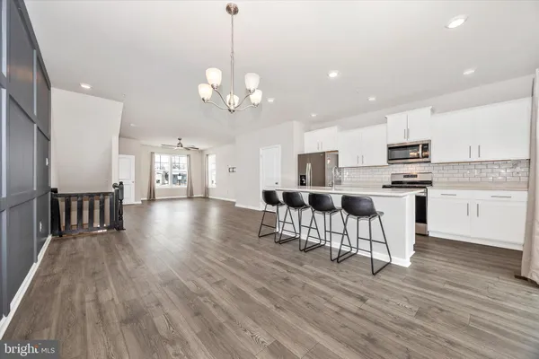 a view of a kitchen with stainless steel appliances granite countertop a stove top oven a refrigerator a dining table and chairs with wooden floor