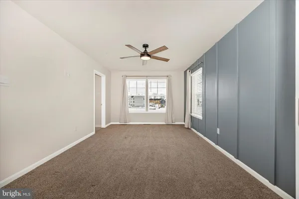 an empty room with chandelier fan and windows
