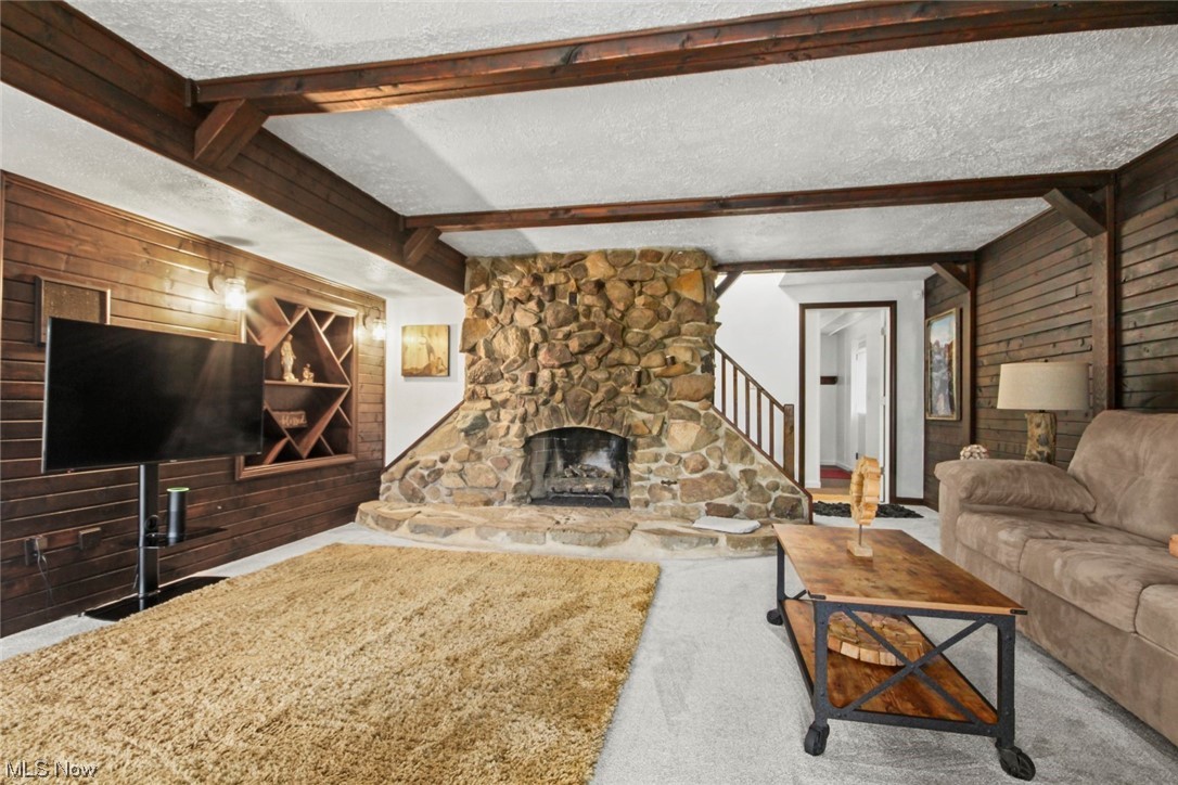 7550 South Raccoon Road Canfield, OH 44406 - Photo 8 of 32 Carpeted living room featuring a fireplace, wooden walls, a textured ceiling, and beam ceiling