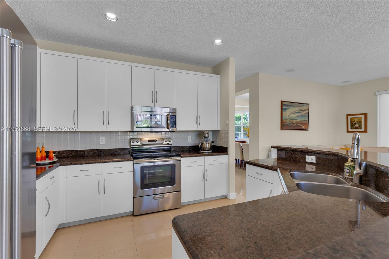 4441 Stone Ridge Way Weston, FL 33331 - Photo 25 of 87 a kitchen with stainless steel appliances granite countertop a stove top oven a sink a dining table and chairs with white cabinets