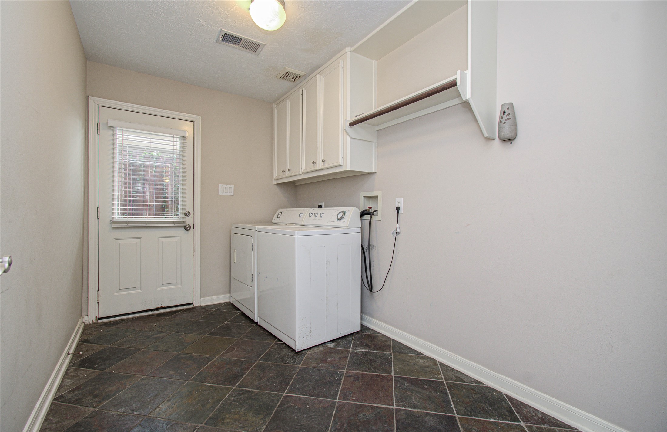 2304 Jackson Street Houston, TX 77004 - Photo 6 of 31 Laundry room features slate tile flooring, washer and dryer, overhead cabinets and extra space for storage. Back door with window offers natural light and leads to the patio.